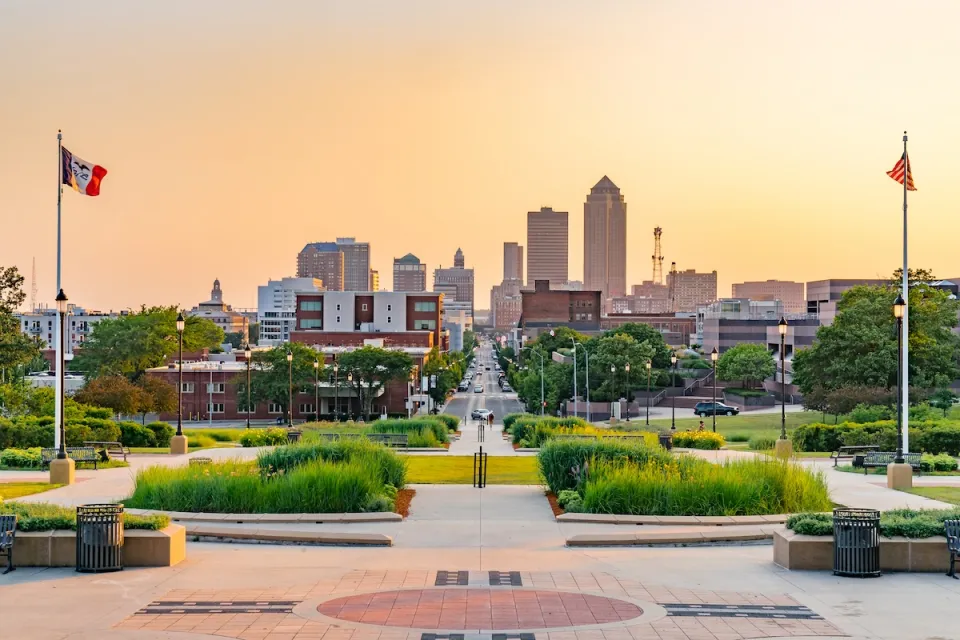 Des Moines, Iowa skyline viewed from a plaza with two flags on either side at dusk.